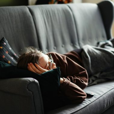 woman in pink jacket lying on gray couch