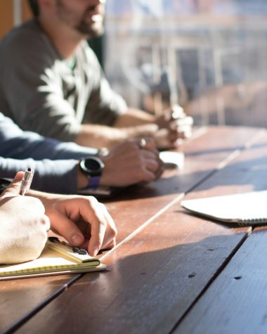 people sitting on chair in front of table while holding pens during daytime