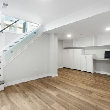 an empty room with a desk, computer, and stairs